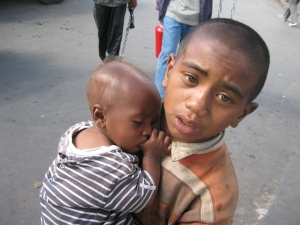 A street boy carries an infant while begging from motorists in the streets of Antanananarivo.